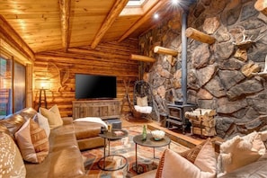 A log cabin interior with a stone wall, wooden furniture, a fireplace, and a television.