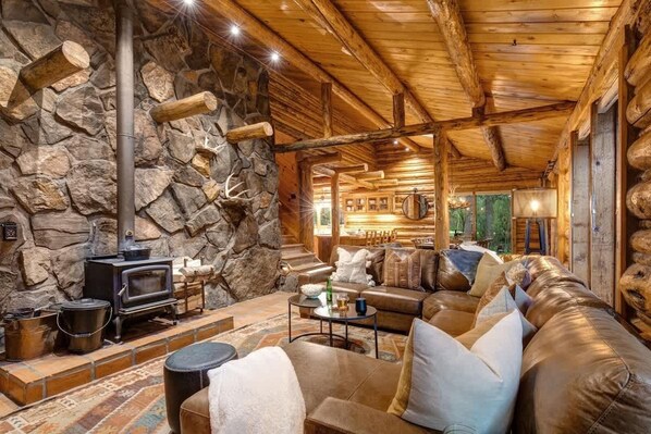 A log cabin interior with a stone wall, a fireplace, leather furniture, and a cozy atmosphere.