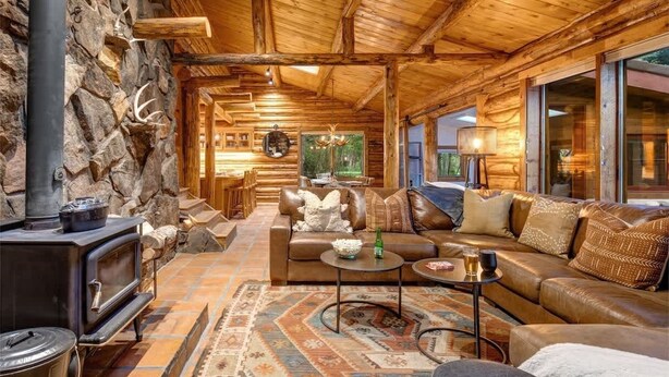A log cabin interior with a stone wall, a wood-burning stove, leather furniture, and a large window. - Abode at the Aspens, hot tub, near Teton Village (Wilson)