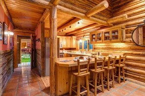 A log cabin interior with a central bar area, wooden walls, and a tiled floor.