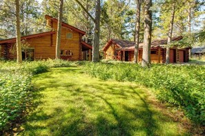 A log cabin with a porch, surrounded by trees and a grassy area.