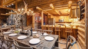 A rustic cabin interior with a stone wall, wooden dining table, chairs, and a kitchen area. - Abode at the Aspens, hot tub, near Teton Village (Wilson)