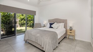 Quarto moderno com cama grande, porta de vidro deslizante para um jardim e mesa de cabeceira com luminária.