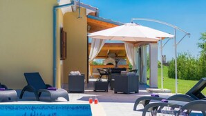 Un espace piscine comprenant des chaises longues, une table et un coin salon abrité.