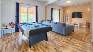 Une table de billard dans un salon, avec un canapé et un téléviseur.