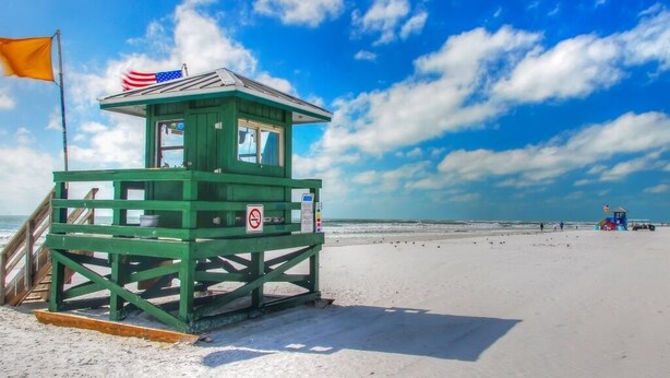 A lifeguard tower with a flag, situated on a sandy beach with a clear sky.