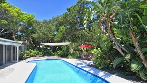 A swimming pool surrounded by lush greenery and a covered patio area with chairs.