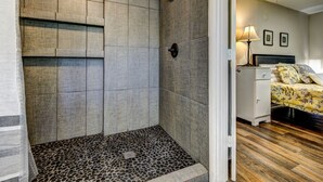 A bathroom with a shower area and a bedroom with a bed and nightstand.