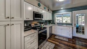 A kitchen with white cabinets, a microwave, oven, and a sink. There are decorative plates on the wall and a window with a view of greenery outside.