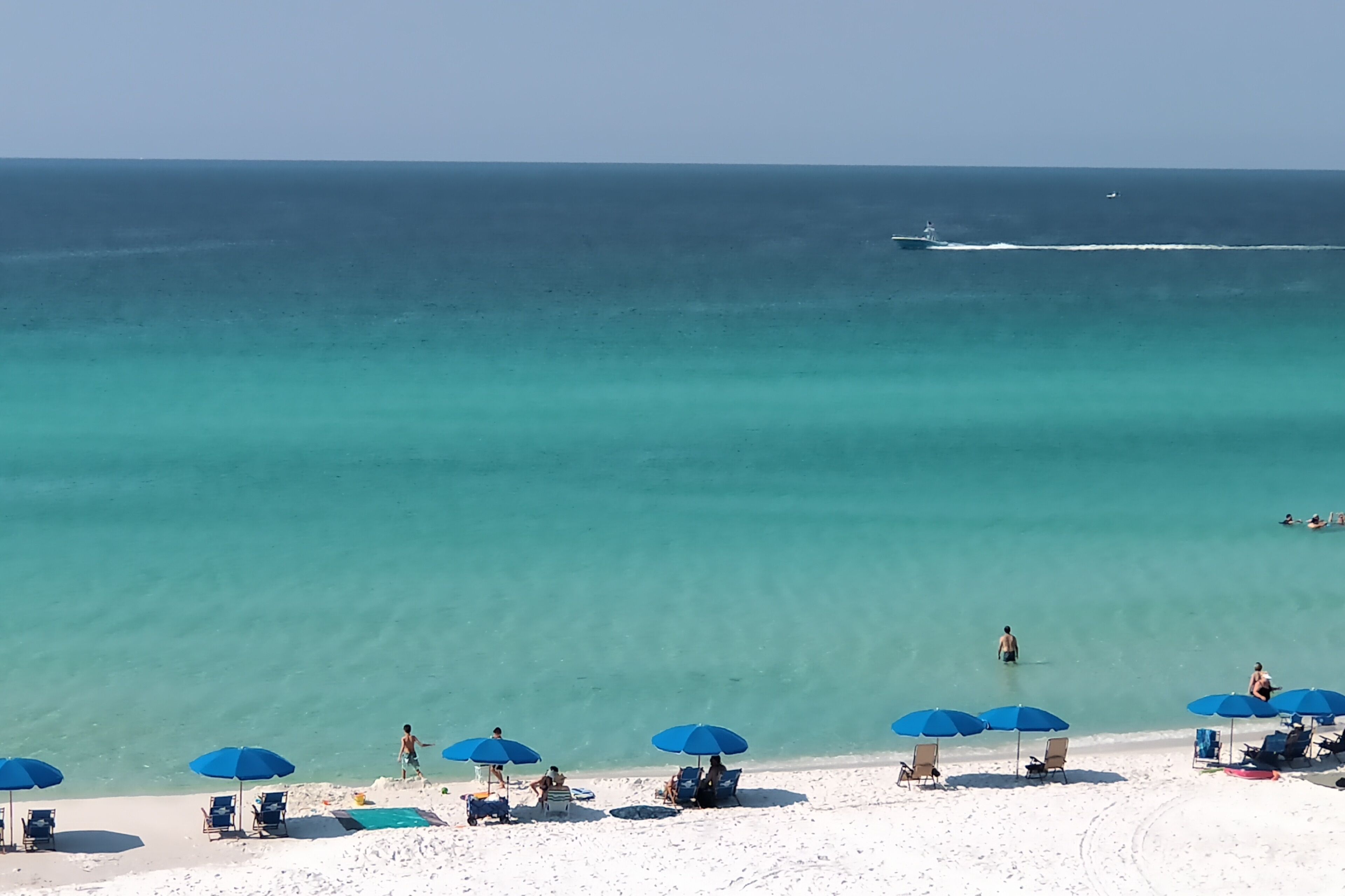 A beach with clear turquoise water, white sand, and blue umbrellas.
