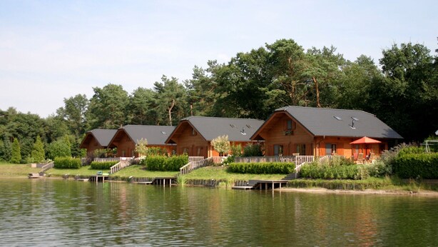 A row of wooden cabins with a dock extending into a calm lake, surrounded by lush greenery. - Tidy Holiday Home in the Achterhoek (Lochem)