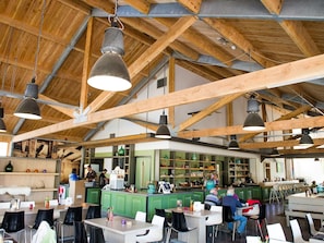 A spacious café with high wooden beams and pendant lighting.