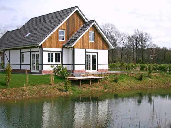 A two-story house with a sloped roof, a wooden exterior, and a brick foundation. It is situated next to a body of water with a small dock extending into the water.