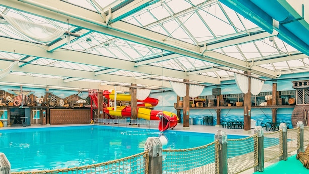 An indoor swimming pool with a slide, netted safety barriers, and a wooden deck area. - Chalet Near Zuiderzee With Garden (Biddinghuizen)