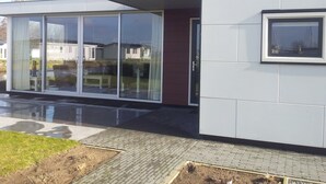 Un edificio moderno con grandes puertas correderas de vidrio, un ventanal pequeño y un área de entrada pavimentada.