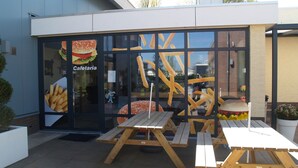 Un área de estar al aire libre con mesas y bancos de madera frente a un edificio con fachada de vidrio que muestra imágenes de comida.