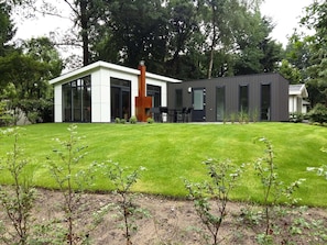 A modern house with a large lawn, a dining area with chairs, and a tall chimney. - Bright Chalet in the Achterhoek (Lochem)