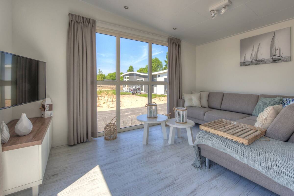 Ein modernes Wohnzimmer mit großem Fenster, einem Flachbildfernseher, einer Couch und einem kleinen Tisch.
