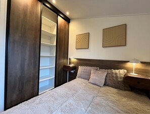 Una camera da letto con un letto, un comodino, una lampada, un armadio e due elementi decorativi appesi alle pareti.
