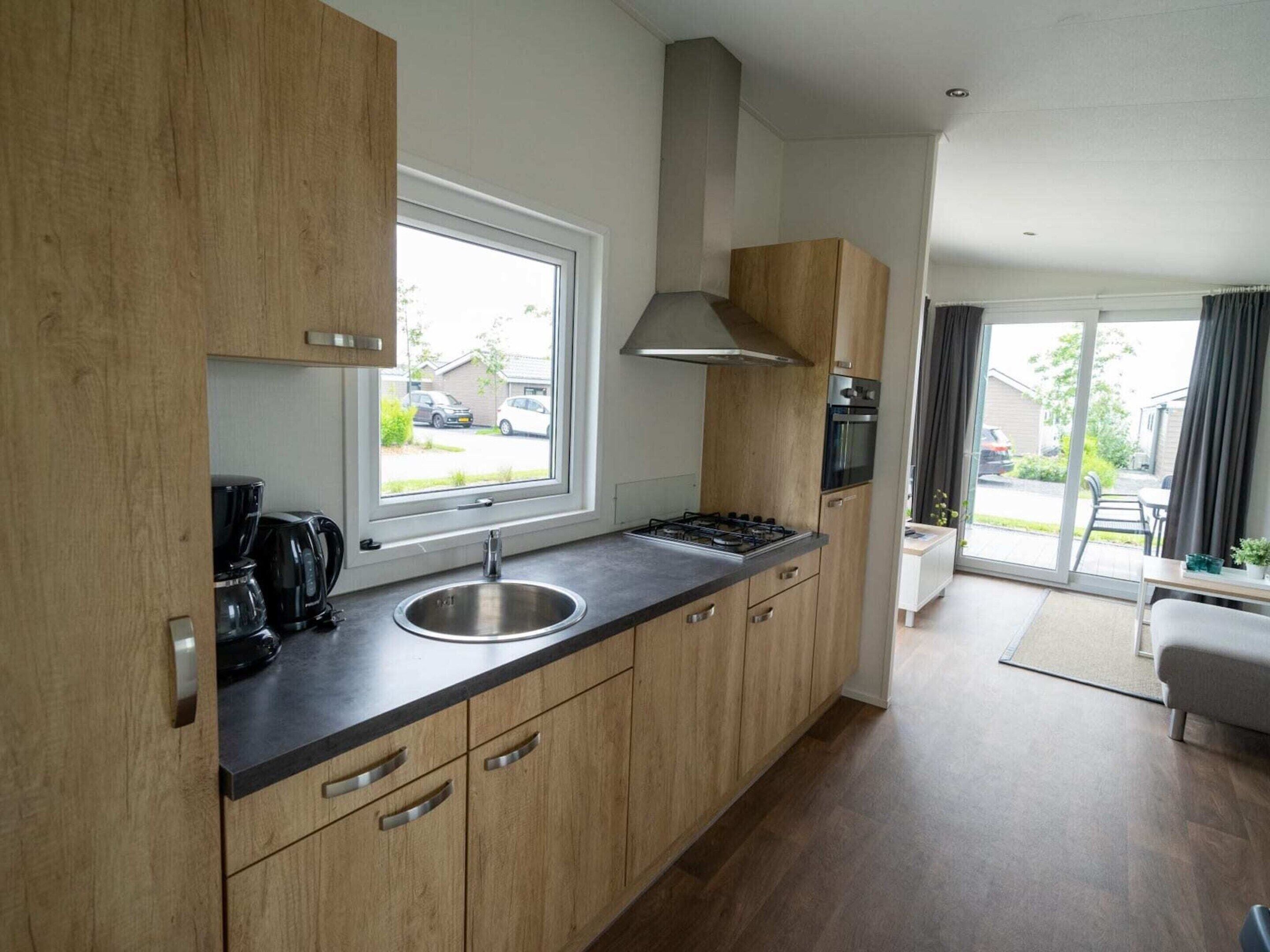 Een moderne keuken met houten kasten, een roestvrijstalen spoelbak en een raam met uitzicht op een woonwijk.