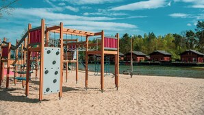 A playground with climbing structures and swings, set against a backdrop of a river and red buildings. - Tidy Holiday Home With Dishwasher (Lochem)