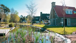 A house with a stone chimney, a pond with water plants, and a well-maintained lawn. - Tidy Holiday Home With Dishwasher (Lochem)