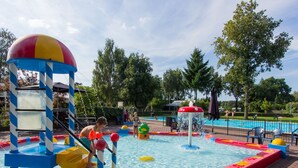 Ein Wasserspielbereich mit Rutschen und Wassereffekten, umgeben von einem Pool und Bäumen.