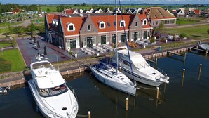 Un port de plaisance avec deux bateaux amarrés, un bâtiment avec un toit rouge et une zone herbeuse avec un chemin menant à ce bâtiment.