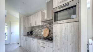 Una cucina moderna con mobili in legno chiaro, zoccolo in pietra e elettrodomestici in acciaio inossidabile.