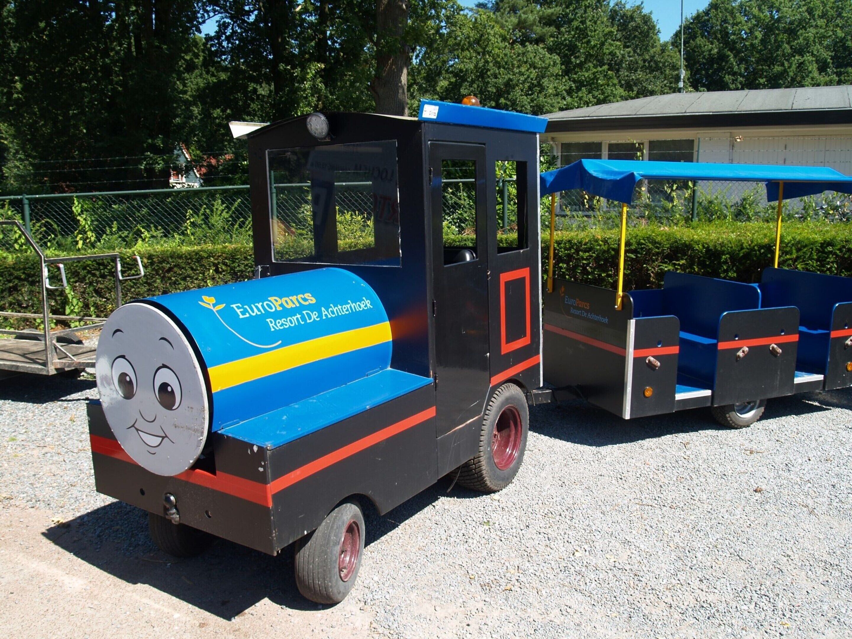 A EuroParcs Resort De Achterhoek train with a smiling face on the front, parked on a gravel surface.