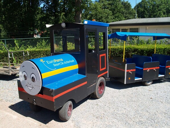 Et tog fra EuroParcs Resort De Achterhoek med et smilende ansigt foran, parkeret på en grusoverflade.