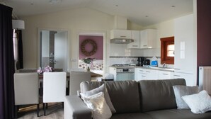 A modern living room with a sofa, a dining table, and a kitchen in the background. - Wooden Chalet Located in the Achterhoek (Lochem)