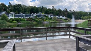 A wooden deck with a view of modern buildings and a fountain by a lake. - Modern Holiday Home Near Brunssummerheide (Brunssum)