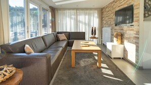 A modern living room with a sectional sofa, a wooden coffee table, and a large window offering a view of the outdoors. - Modern Holiday Home Near Brunssummerheide (Brunssum)