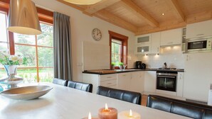 A modern kitchen with white cabinets, a microwave, and an oven. There is a dining table with candles and a vase of flowers. - Wooden Holiday Home Near Brunssummerheide (Brunssum)