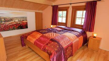 Ein Schlafzimmer mit einem großen Bett, Holzböden, einem Bild an der Wand und zwei mit Vorhängen versehenen Fenstern.