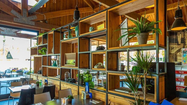 A restaurant with wooden shelves and tables, featuring various items like plants and kitchenware. - Modern Chalet Near De Veluwe National Park (Otterlo)