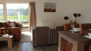 A spacious living area with a sofa, armchairs, and a dining table. A large window offers a view of a green landscape. - Comfortable Chalet With Dishwasher (IJhorst)