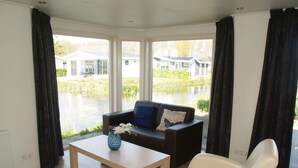 A living room with a sofa, a coffee table, and a chair. There is a window with a view of a house and a body of water. - Comfortable Chalet With Dishwasher (IJhorst)