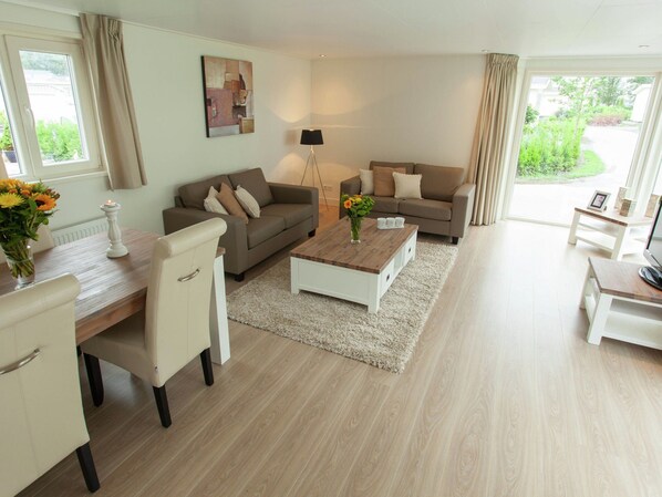 A modern living room with two sofas, a coffee table, a dining table with chairs, and a lamp. - Comfortable Chalet With Dishwasher (IJhorst)