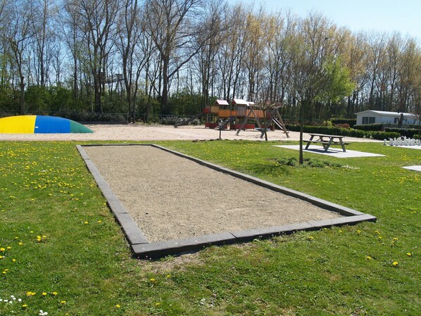Ein Spielplatz mit Sandkasten und Schaukeln, umgeben von Bäumen und einem Picknicktisch.