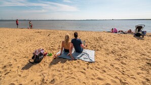 A sandy beach with people relaxing and a stroller in the foreground.