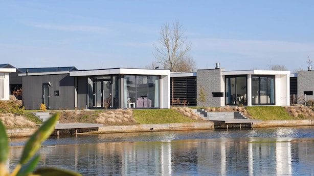 Un complexe résidentiel moderne à l’architecture contemporaine, caractérisé par de grandes baies vitrées et un plan d’eau paisible en premier plan.