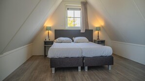 A bedroom with a sloped ceiling, two bedside tables with lamps, a bed with two pillows, and a window with a curtain. - Dutch Family Geataway in West-graftdijk (West-Graftdijk)
