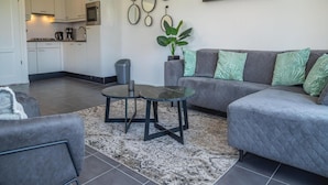 A modern living room with a grey sofa, a round coffee table, and a kitchen in the background. - Dutch Family Geataway in West-graftdijk (West-Graftdijk)