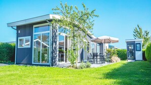 Ein modernes Haus mit Terrasse, einem kleinen Baum und blauem Himmel.