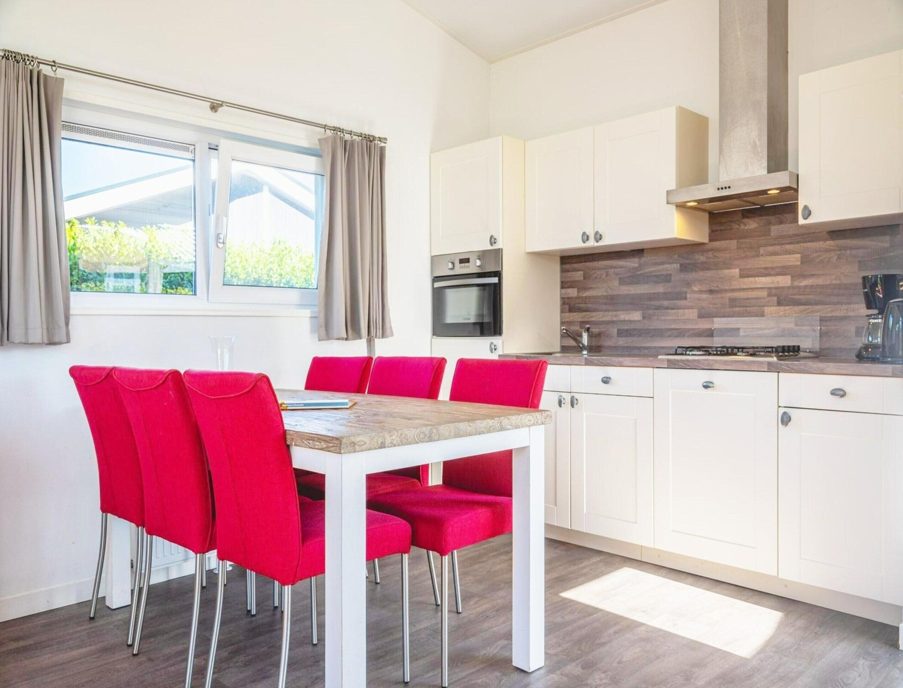 A modern kitchen with white cabinets, a wooden countertop, and a red dining table with matching chairs.