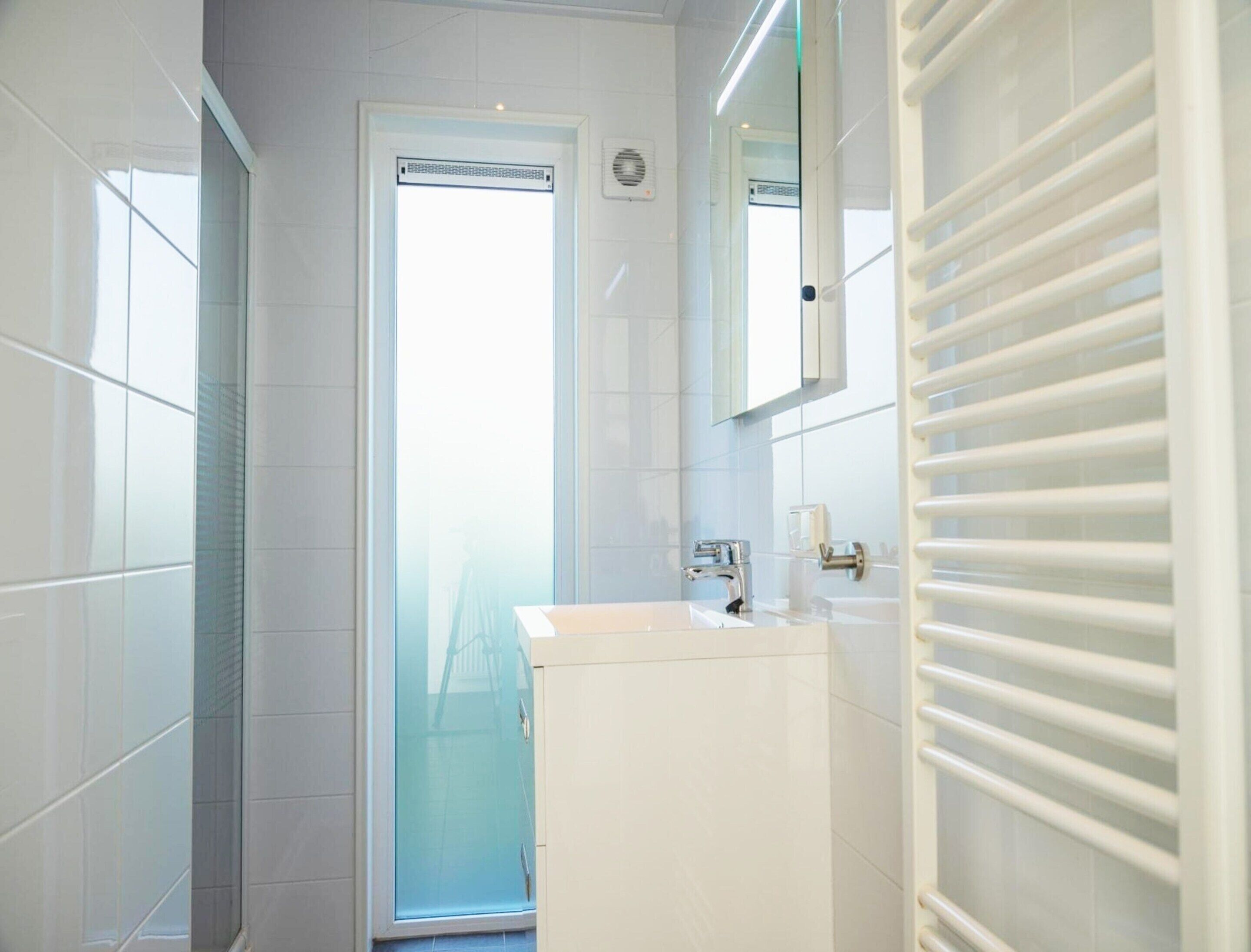 Une salle de bain avec un lavabo blanc, un miroir et une fenêtre en verre dépoli.