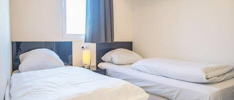 A hotel room with two beds, a window with curtains, a bedside lamp, and a dark-colored wardrobe.