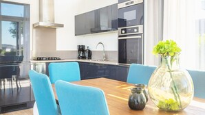 Eine moderne Küche mit schwarzen Schränken, einem Herd und einer Kaffeemaschine. Ein Esstisch mit blauen Stühlen und eine Vase mit grünen Blumen sind ebenfalls vorhanden.